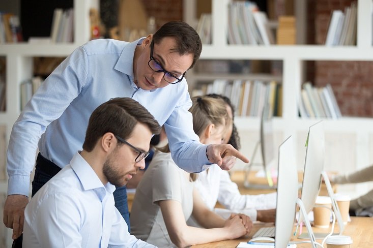 Angry boss criticizing scolding sad male employee for computer mistake